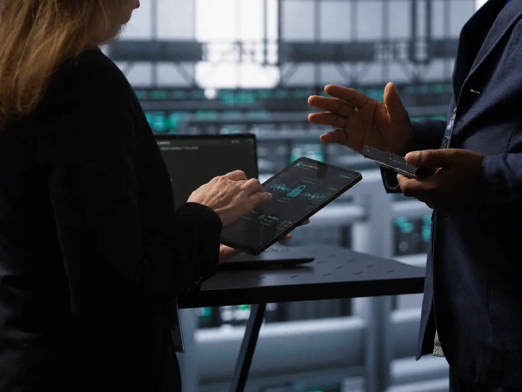 Deux intervenants examinant un tableau de bord de sécurité sur une tablette, en salle serveurs