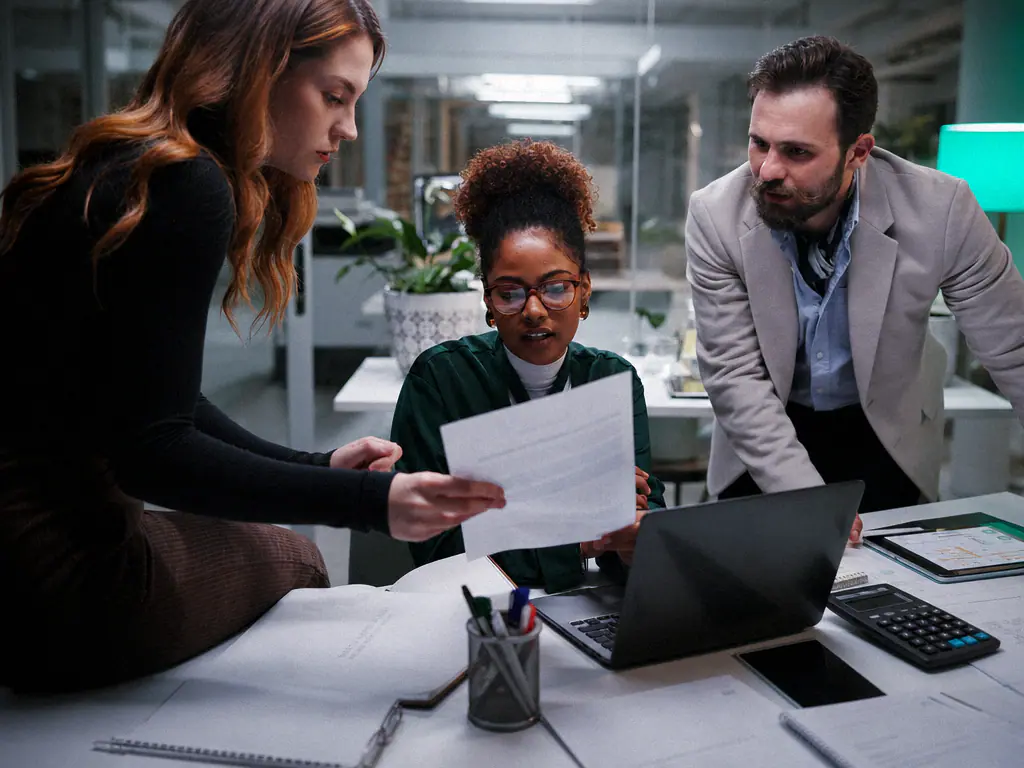 Trois collaborateurs comparant une facture papier et des documents autour d’une table