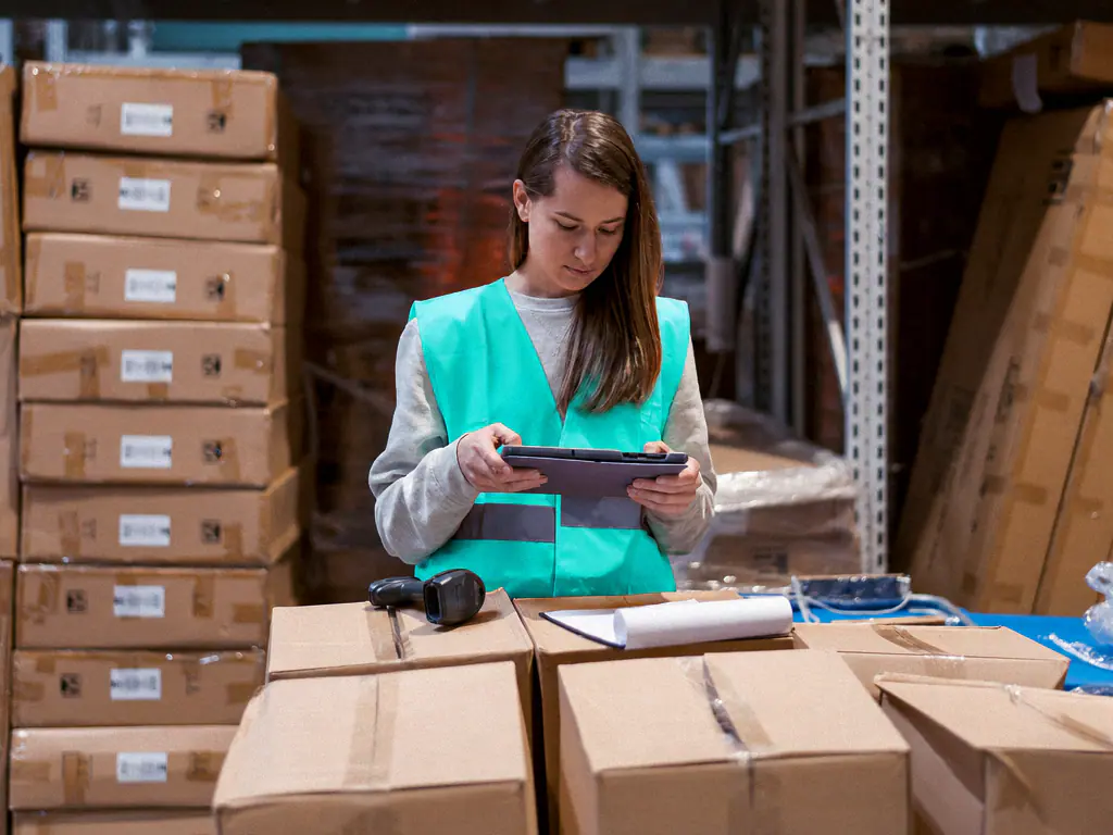 Préparatrice de commandes en gilet de sécurité relevant un stock sur sa tablette