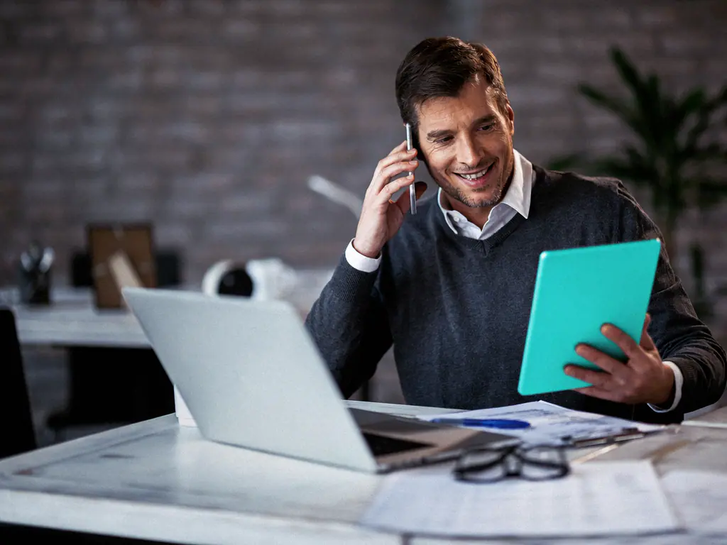 Commercial au téléphone consultant sa tablette à son bureau