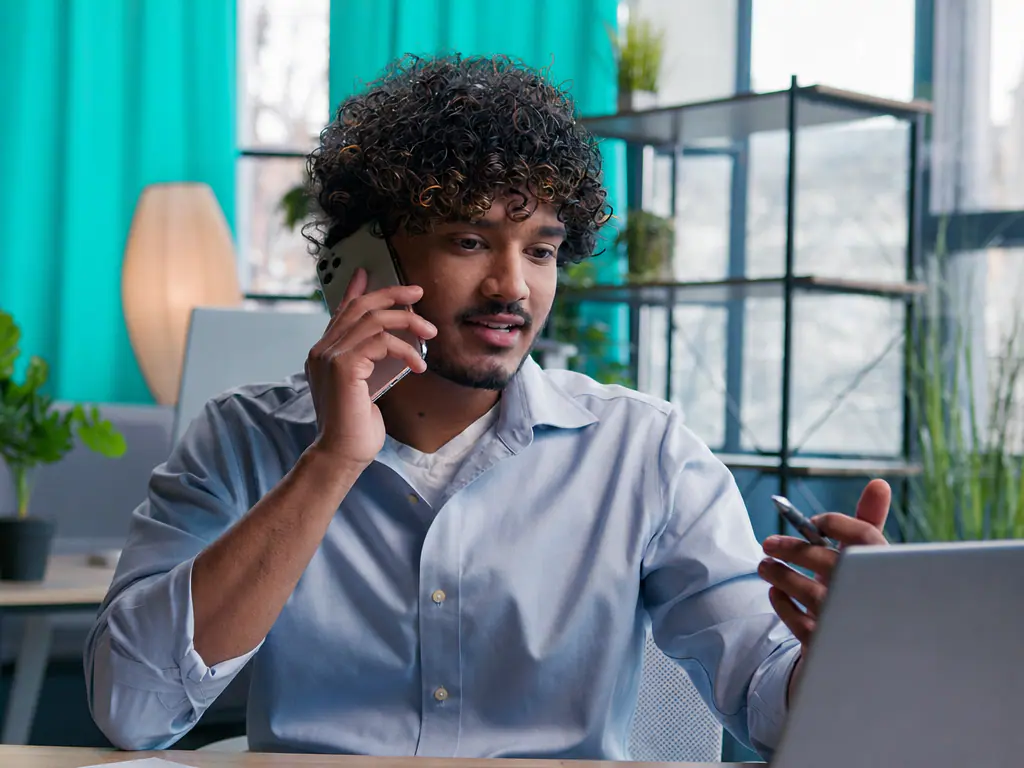 Dirigeant relançant un client au téléphone depuis son bureau, ordinateur portable ouvert