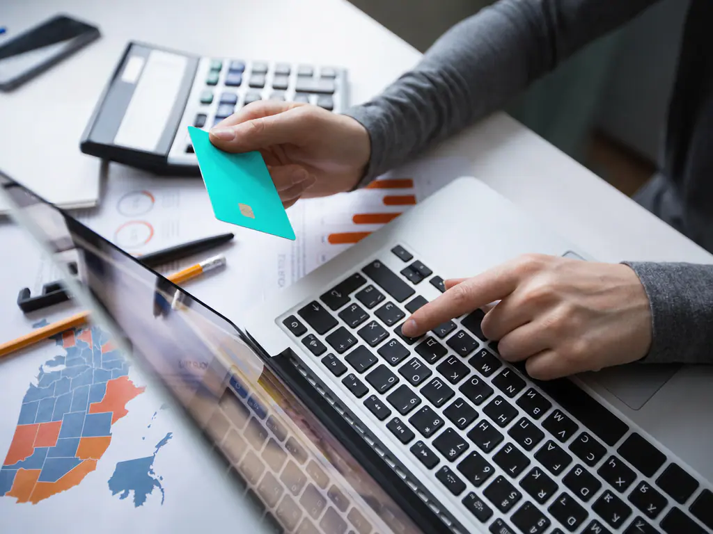Carte bancaire mint tenue au dessus d’un ordinateur portable, calculatrice et graphiques de suivi
