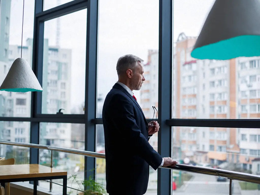Un dirigeant regarde la ville depuis la baie vitrée de son bureau