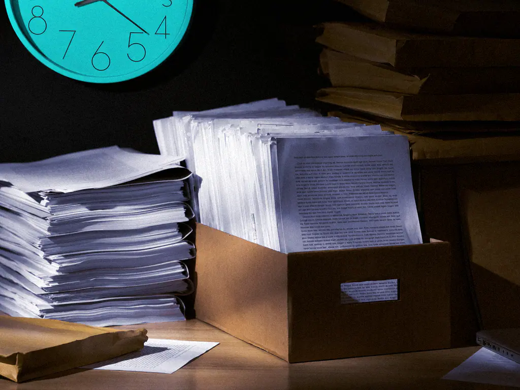 Piles de documents papier et boîte d’archives sur un bureau, une horloge au mur