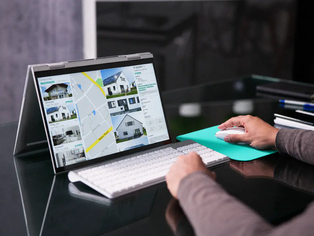 Ordinateur portable affichant des annonces de maisons et une carte, dans une agence