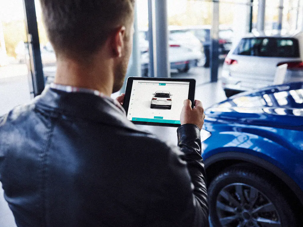 Un conseiller consulte la fiche d’un véhicule sur une tablette dans un showroom automobile