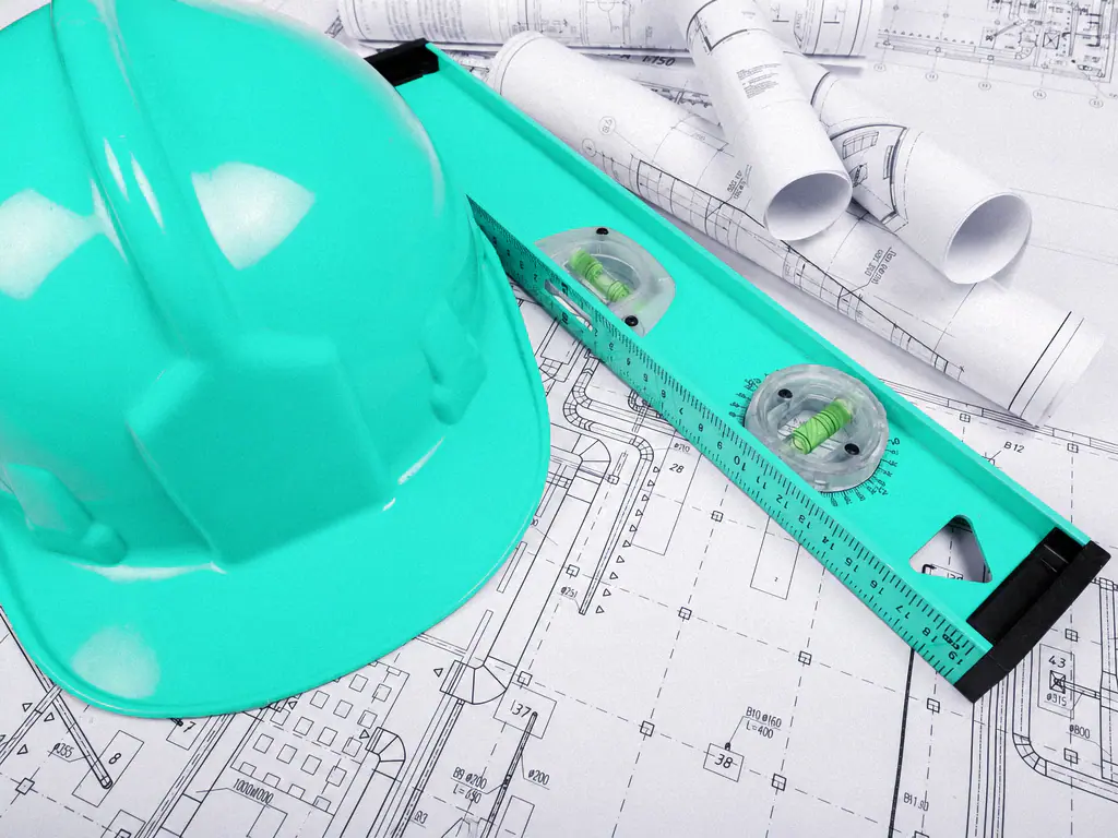 Casque de chantier, niveau et plans de construction posés sur une table