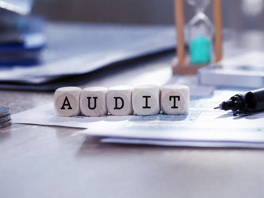 Des dés en bois forment le mot audit posés sur des documents comptables