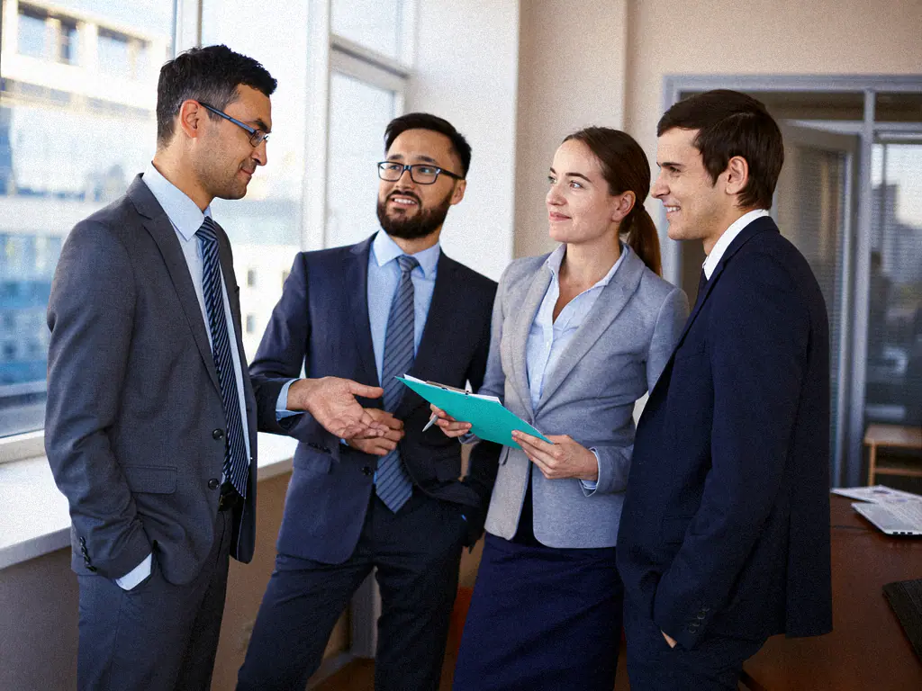 Quatre auditeurs en costume échangent autour d’un classeur dans un bureau