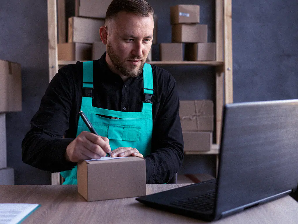 E-commerçant préparant un colis à son bureau devant son ordinateur portable