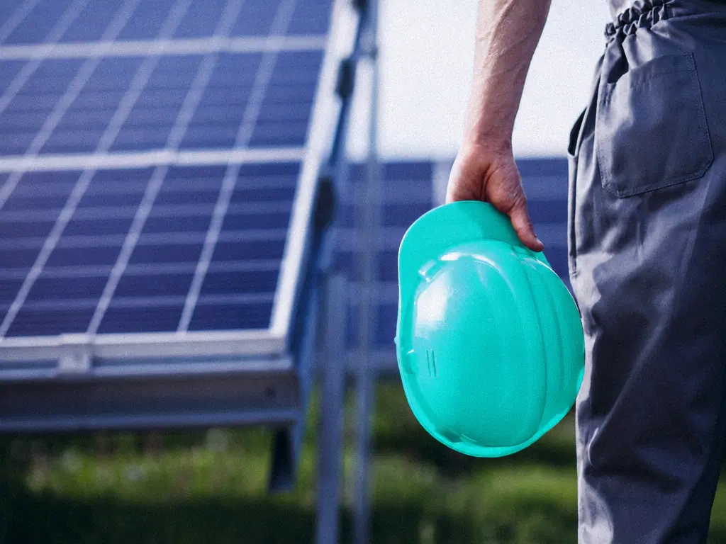 Technicien tenant son casque de chantier devant une rangée de panneaux solaires