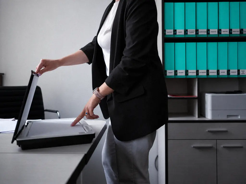 Collaboratrice numérisant un document devant des classeurs étiquetés contrats, clients et archives