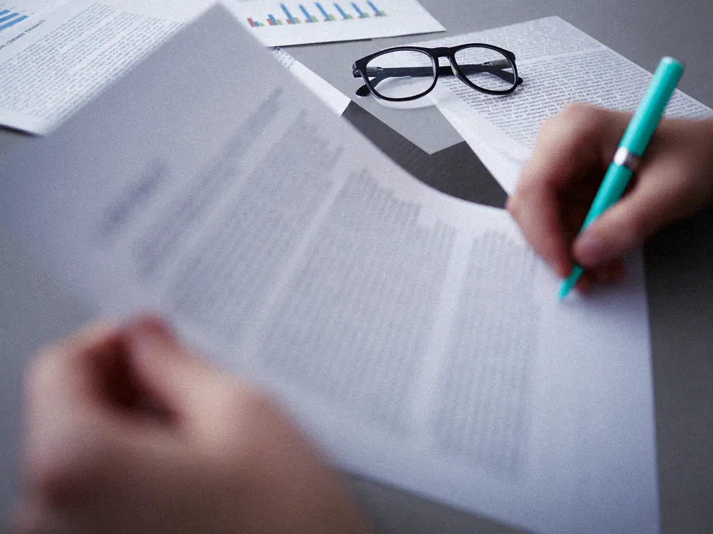 Main annotant au stylo un document juridique imprimé, lunettes posées sur la table