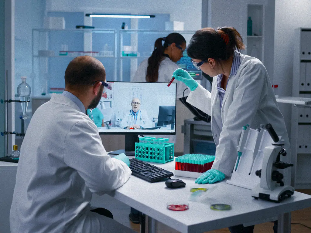 Deux biologistes travaillent à la paillasse pendant une visioconférence avec un confrère