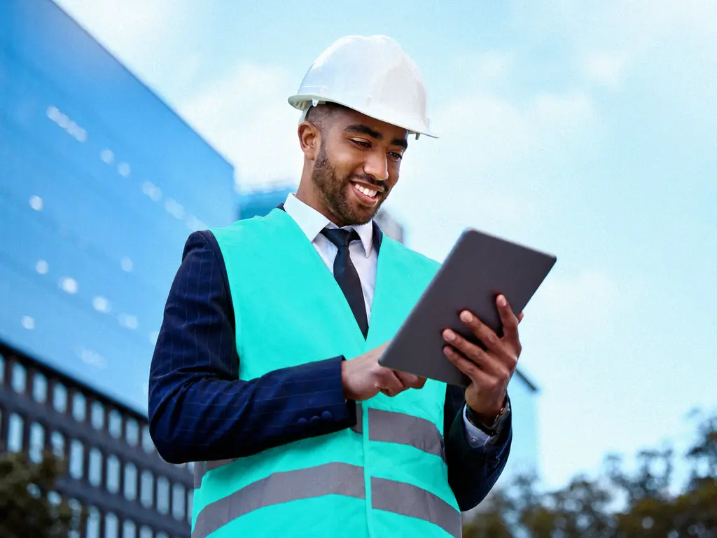 Conducteur de travaux en casque et gilet consultant une tablette devant un immeuble