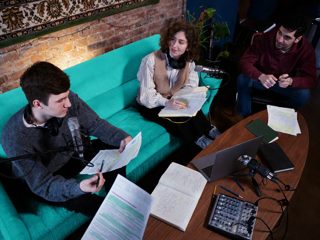 Trois personnes enregistrent un podcast autour d’une table basse couverte de notes