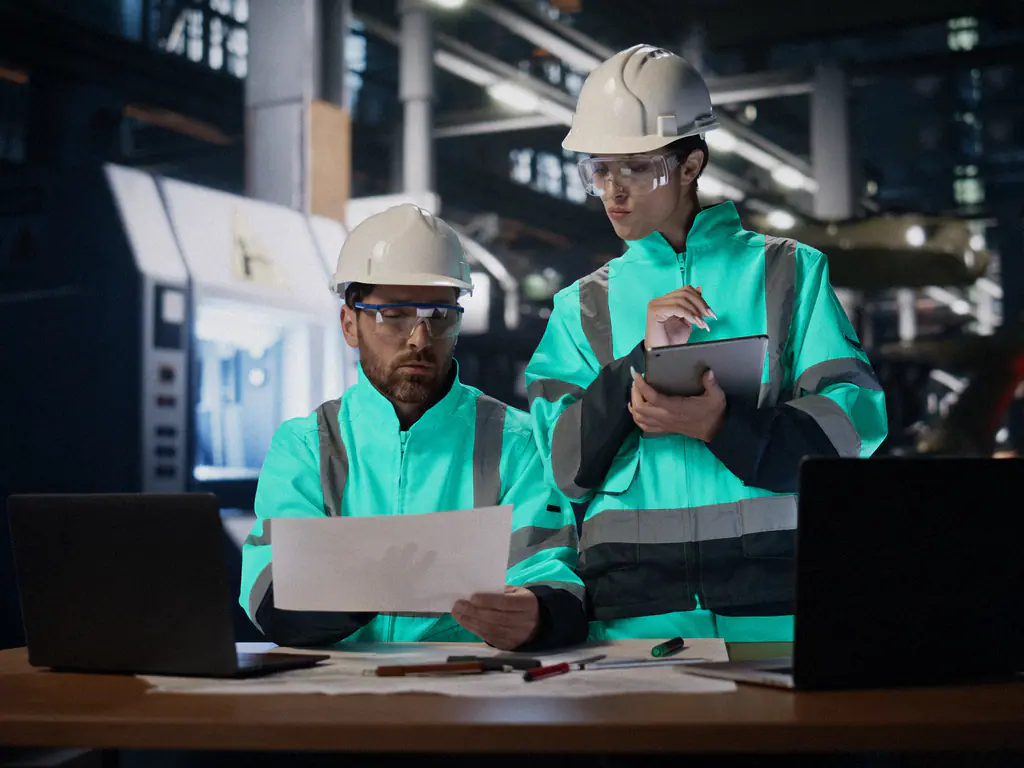 Deux techniciens en gilet relisent une fiche de production devant un poste informatique