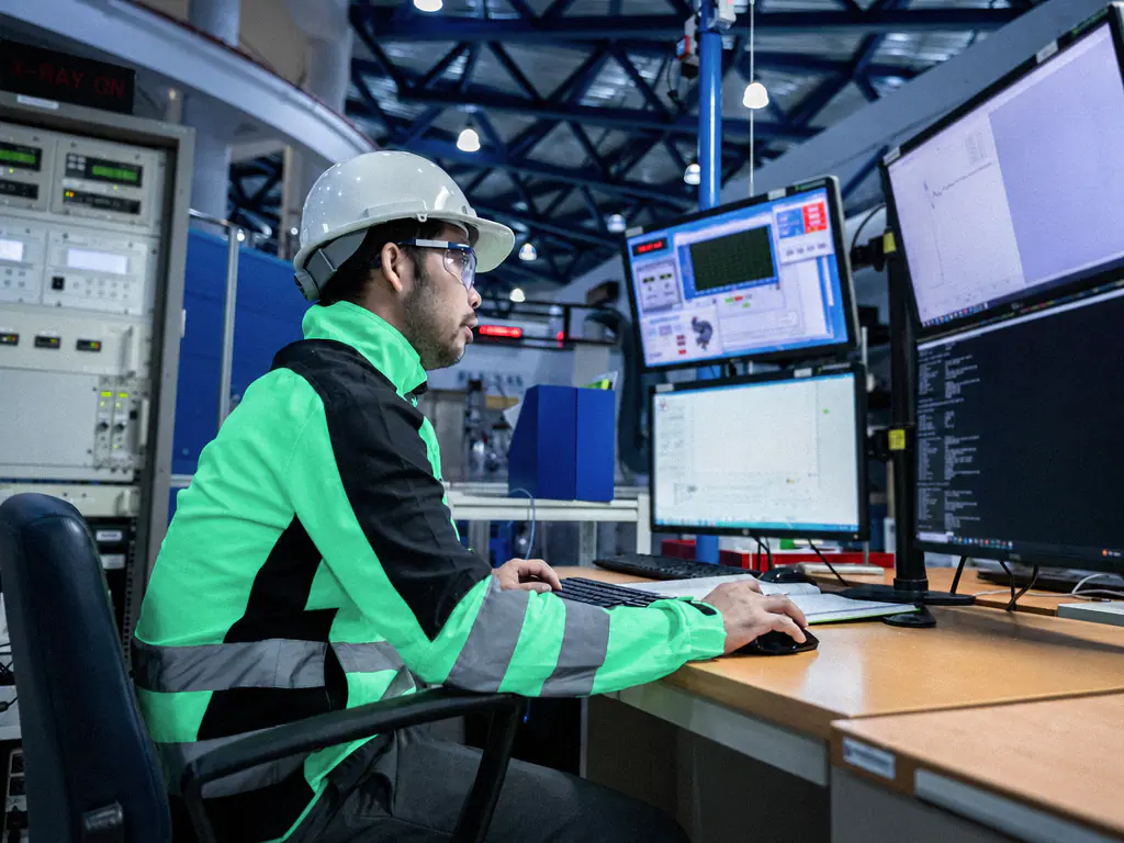Un technicien casqué surveille les paramètres de production sur plusieurs écrans