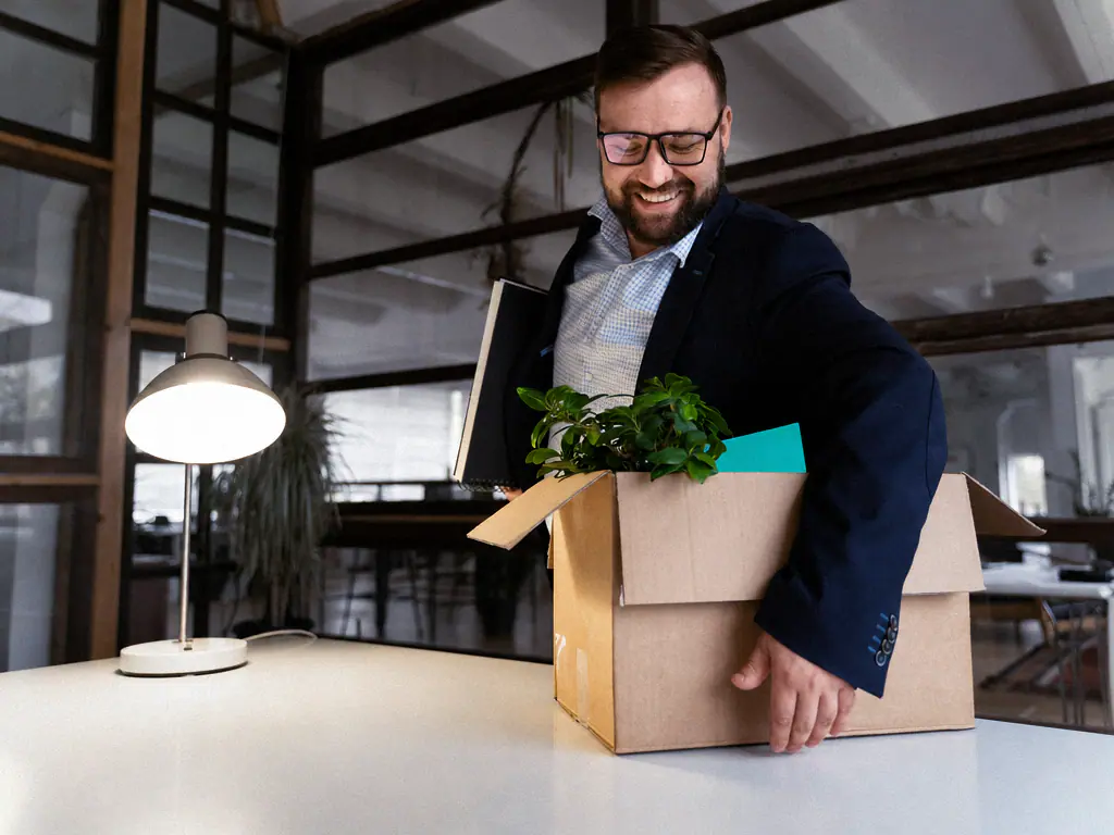 Nouveau collaborateur souriant posant son carton sur son bureau le jour de son arrivée