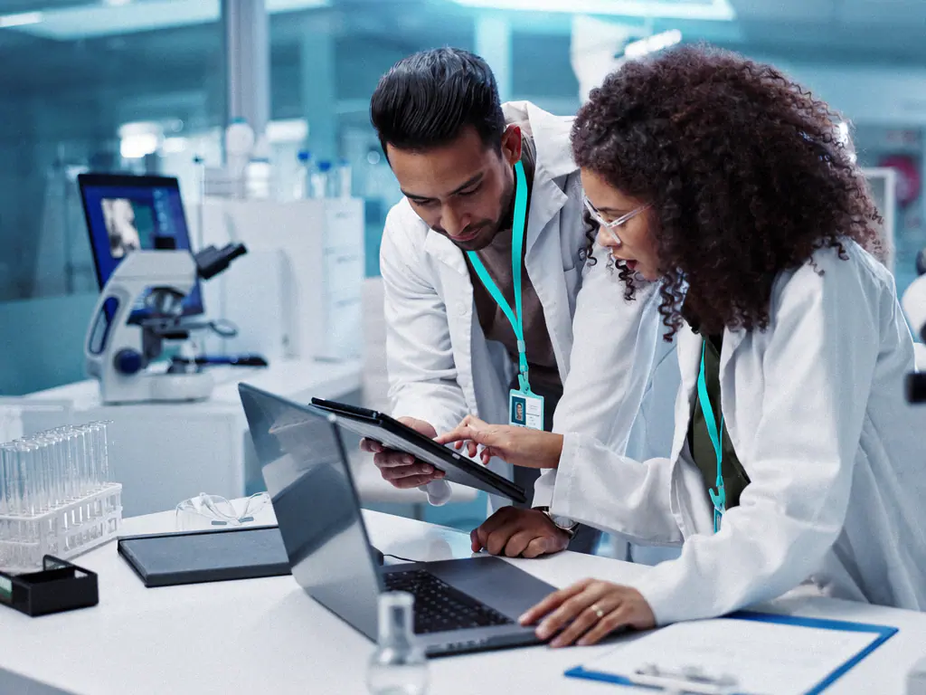 Deux scientifiques en blouse consultent une tablette dans un laboratoire pharmaceutique