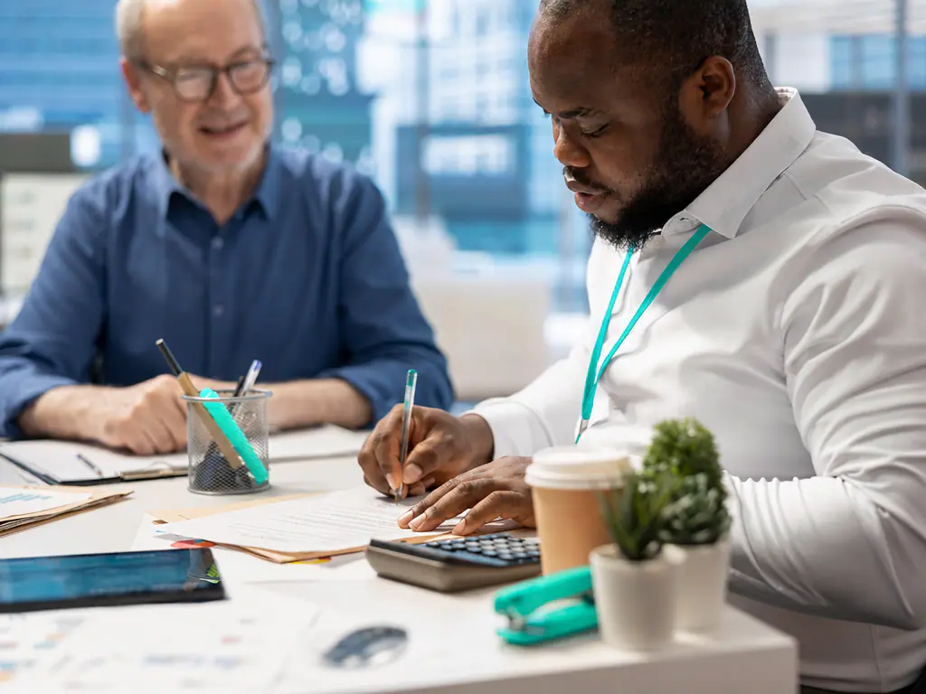 Deux collaborateurs au travail sur des documents financiers, calculatrice sur la table