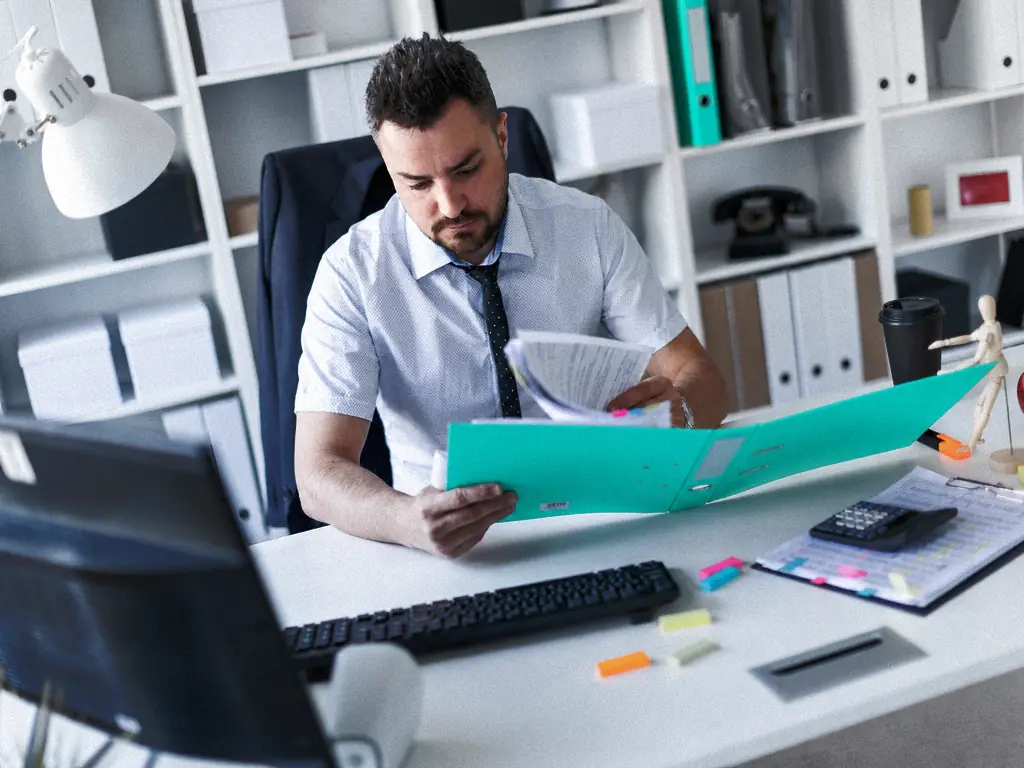 Collaborateur parcourant un dossier de documents à son bureau