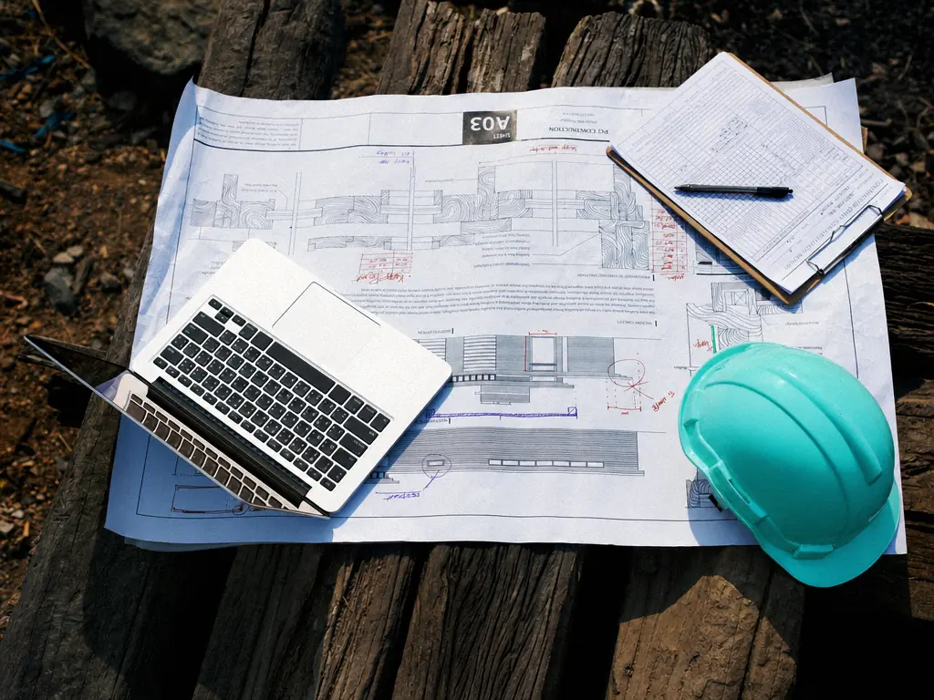 Plans de construction, ordinateur portable et casque de chantier posés sur une table