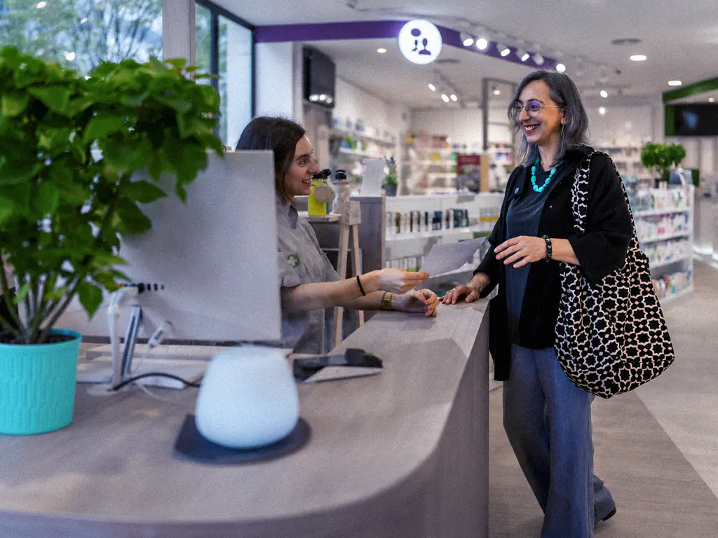Cliente souriante échangeant avec une conseillère au comptoir d’une pharmacie