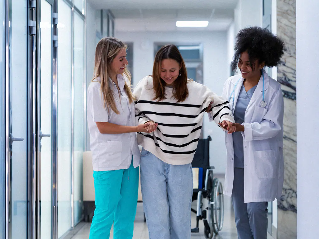 Deux soignantes accompagnent une patiente dans le couloir d’une clinique