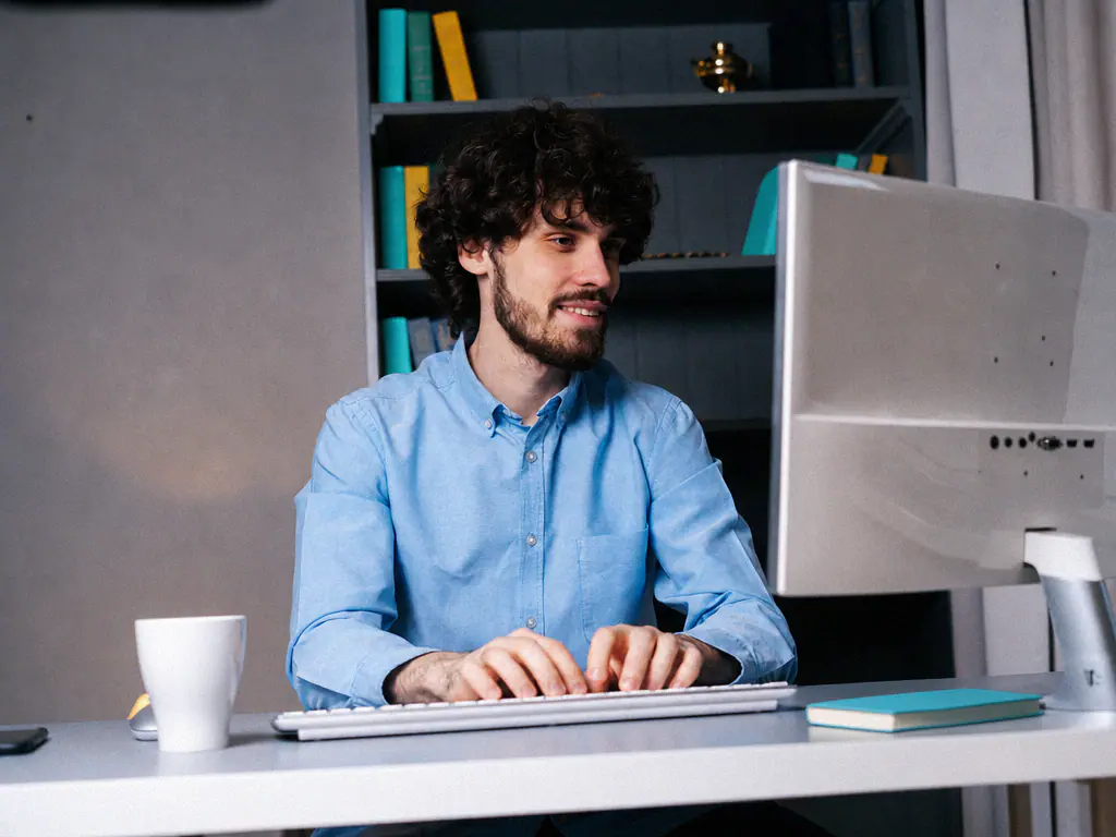 Collaborateur souriant, en train de taper sur le clavier de son ordinateur de bureau