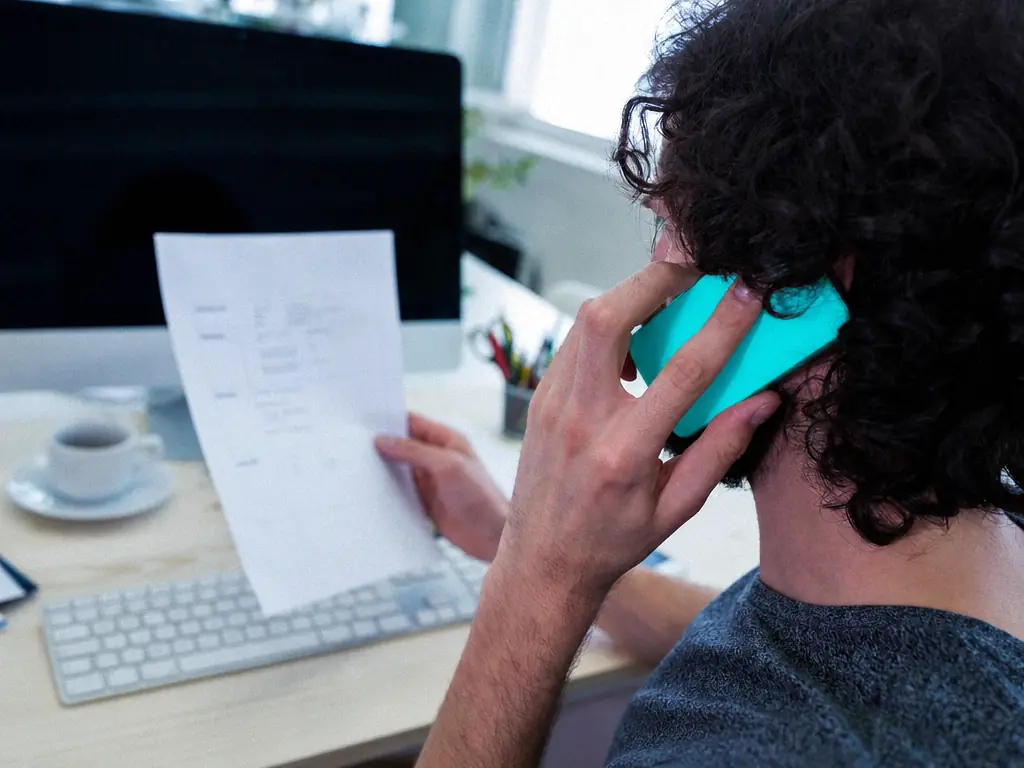 Collaborateur au téléphone, un document à la main, devant son écran