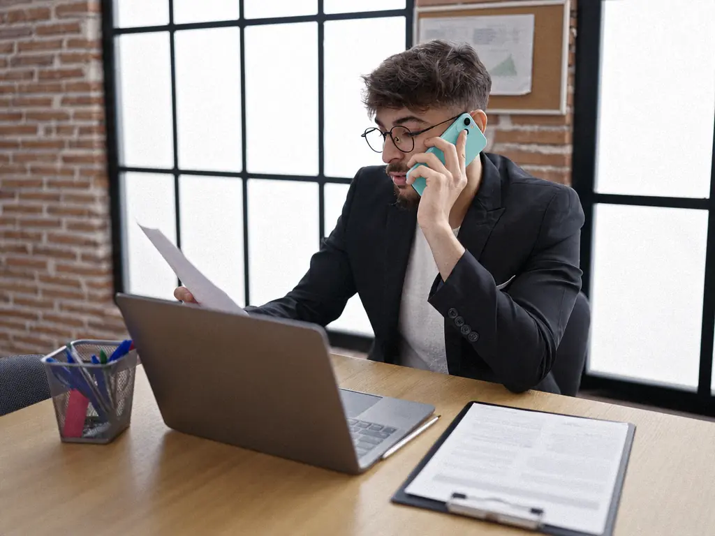 Collaborateur au téléphone devant son ordinateur portable, un contrat posé sur le bureau