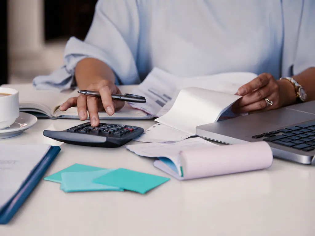 Mains sur une calculatrice à côté d’un carnet et d’un ordinateur portable